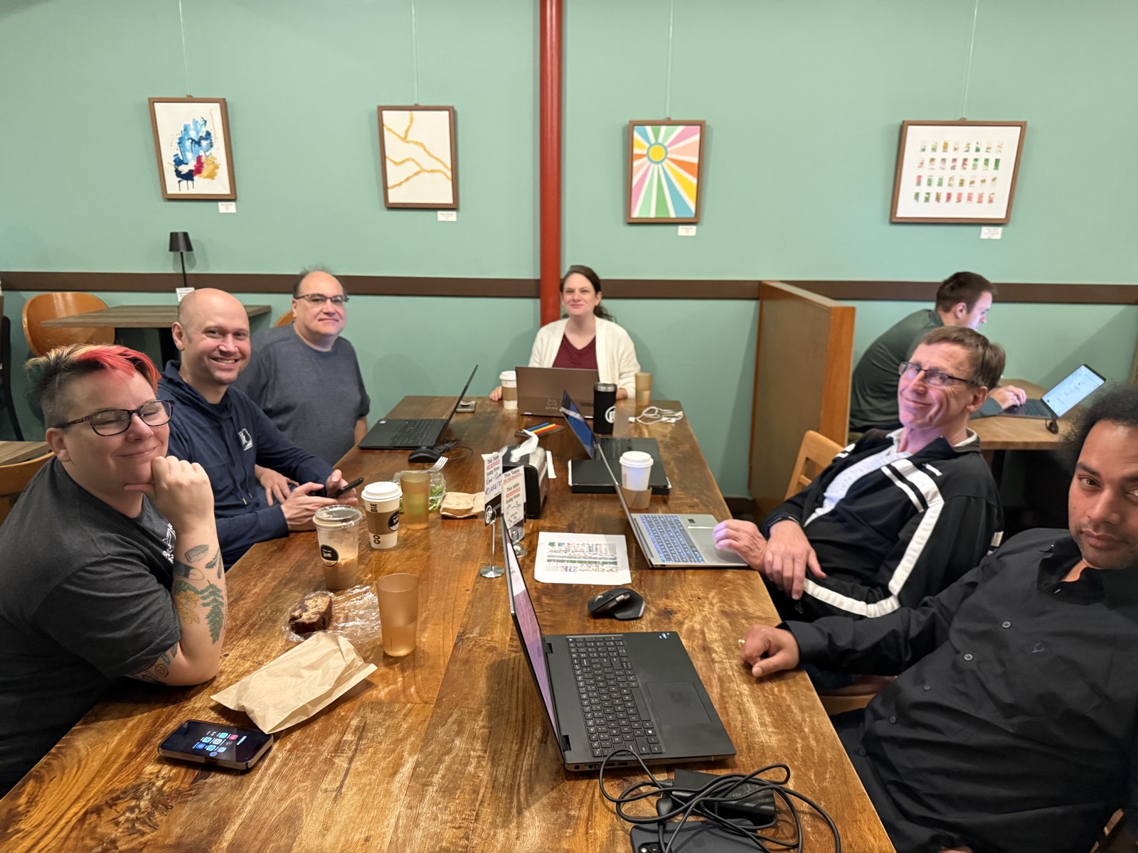 A group of tcplot participants gathered around a long table at The Coffee Shop NE, laptops open, smiling at the camera.