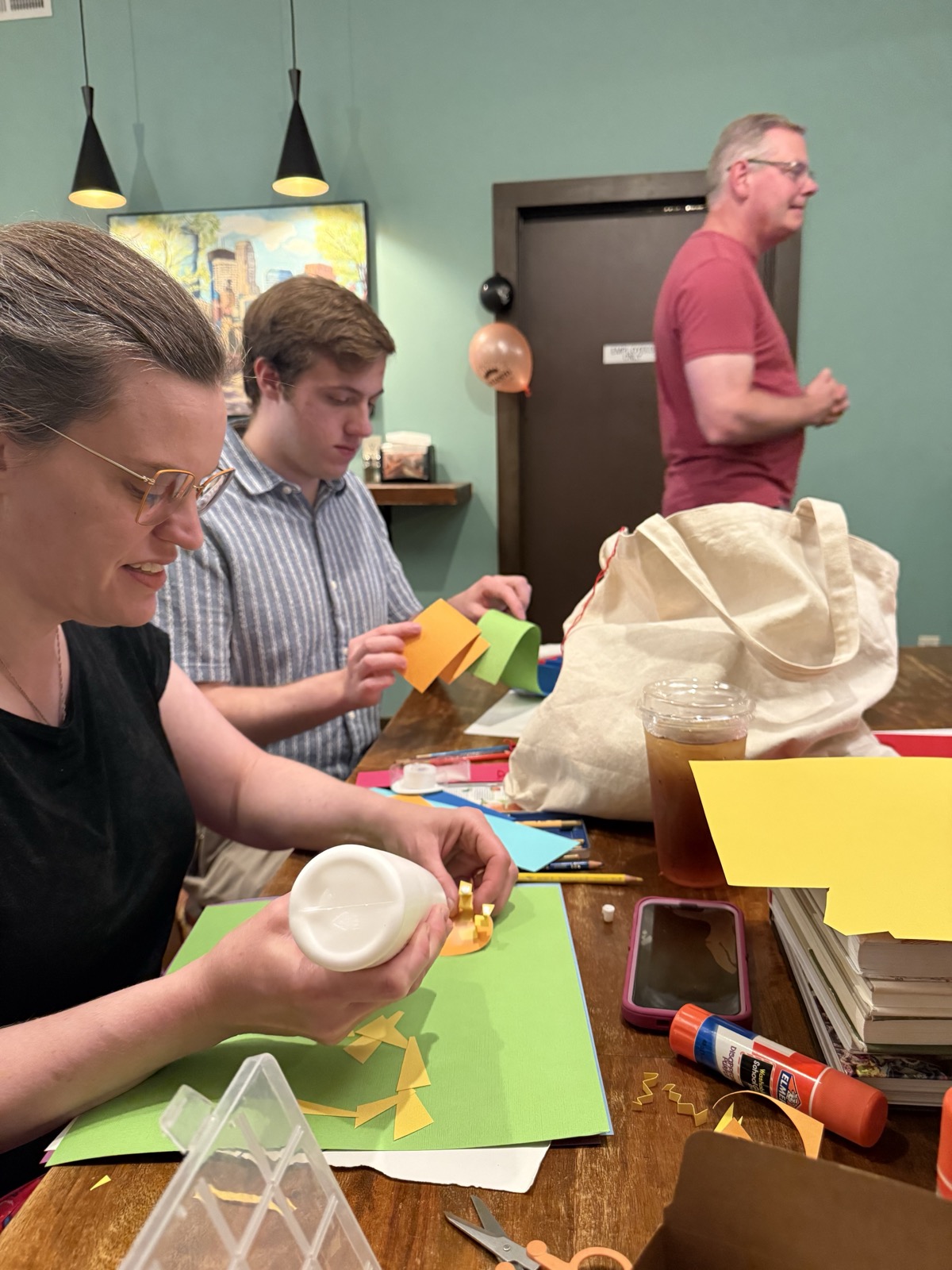 Participants at a table cutting and gluing colored construction paper into physical data artifacts, with glue, scissors, and pencils spread across the table.